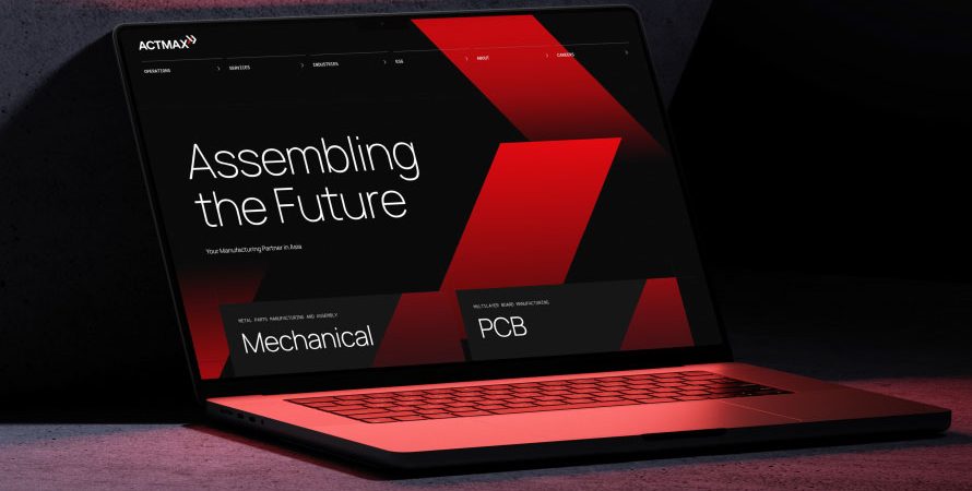 A laptop displaying the Actmax corporate website with bold red geometric designs. The laptop is placed on a textured concrete surface, highlighting an industrial web design created by Bike Bear.